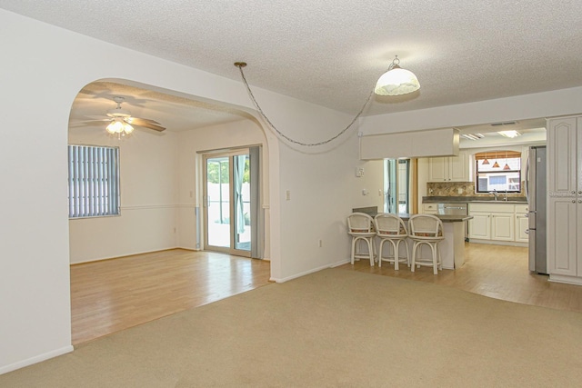living area featuring a textured ceiling, baseboards, light wood finished floors, ceiling fan, and light carpet