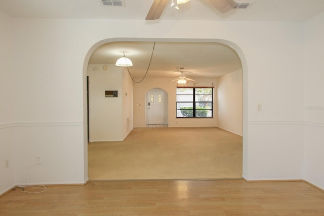 spare room featuring light wood finished floors, arched walkways, a ceiling fan, and visible vents