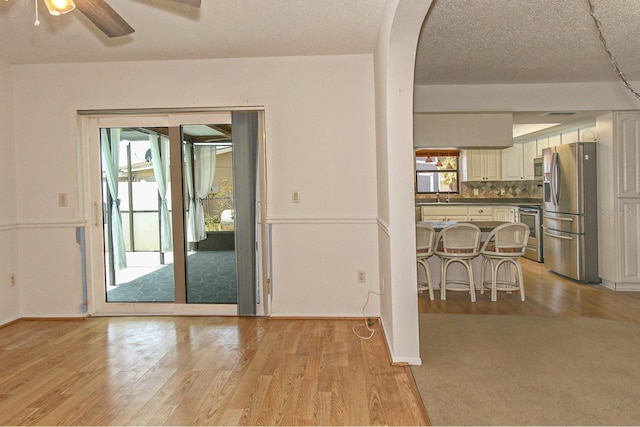 dining room with ceiling fan, a textured ceiling, baseboards, and light wood finished floors