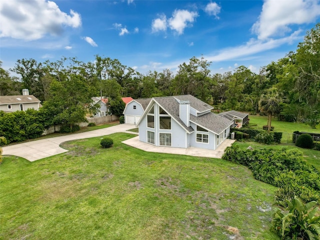 rear view of property featuring fence, a detached garage, concrete driveway, and a lawn