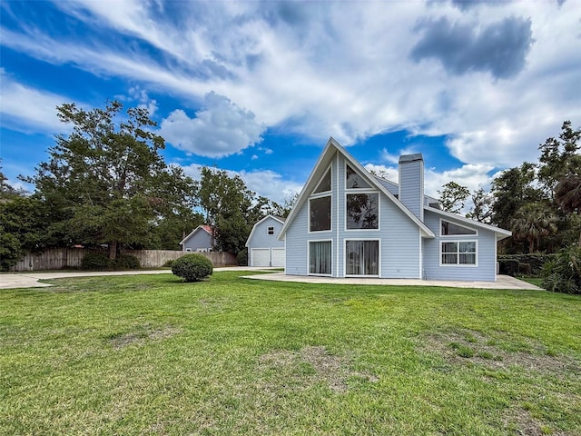 rear view of house featuring a patio, a chimney, a lawn, fence, and a detached garage