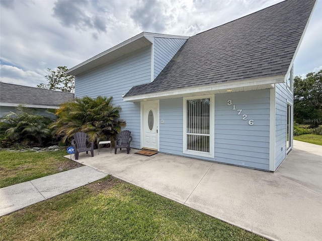 back of property featuring a patio area, roof with shingles, and a lawn