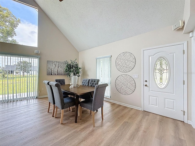 dining space featuring light wood finished floors, a textured ceiling, high vaulted ceiling, and plenty of natural light
