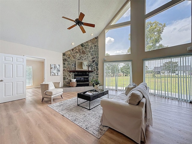 living room featuring wood finished floors, a ceiling fan, high vaulted ceiling, a fireplace, and a textured ceiling