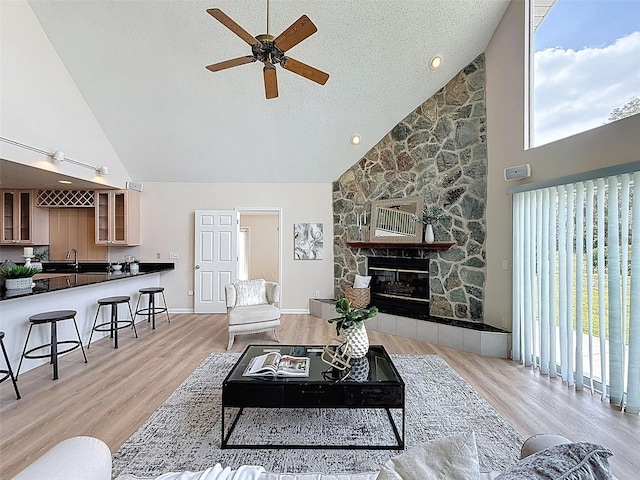 living area featuring a ceiling fan, a fireplace, high vaulted ceiling, and wood finished floors