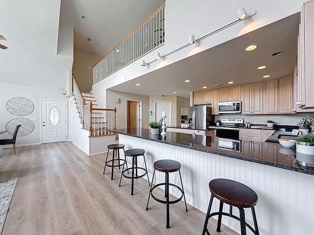 kitchen with a breakfast bar, light wood finished floors, a sink, high vaulted ceiling, and appliances with stainless steel finishes