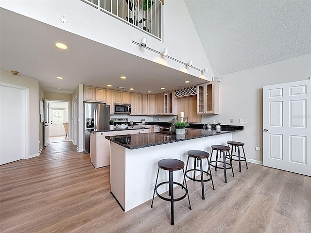 kitchen with appliances with stainless steel finishes, a breakfast bar area, glass insert cabinets, a peninsula, and light wood-type flooring