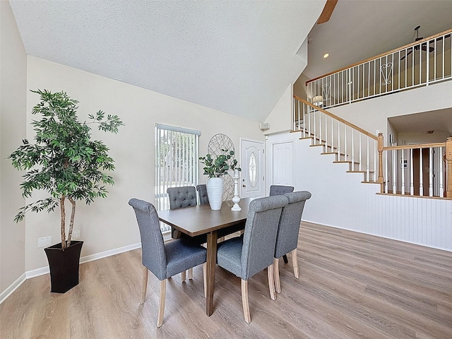 dining area featuring stairs, baseboards, high vaulted ceiling, and wood finished floors