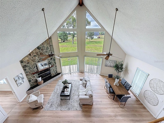living room with wood finished floors, a textured ceiling, high vaulted ceiling, a fireplace, and ceiling fan