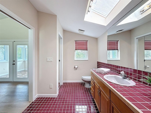 bathroom featuring toilet, baseboards, lofted ceiling with skylight, visible vents, and vanity