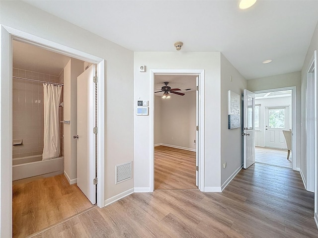 corridor featuring baseboards, light wood finished floors, and visible vents