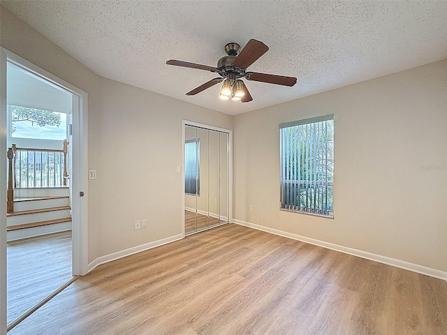 spare room featuring baseboards, light wood-style floors, ceiling fan, and a textured ceiling