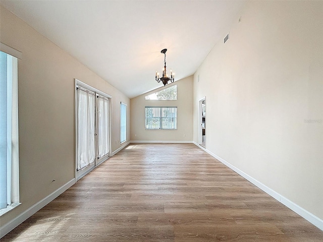 unfurnished dining area featuring wood finished floors, a notable chandelier, visible vents, baseboards, and vaulted ceiling