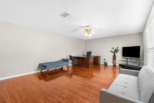 home office featuring a textured ceiling, baseboards, ceiling fan, visible vents, and wood finished floors
