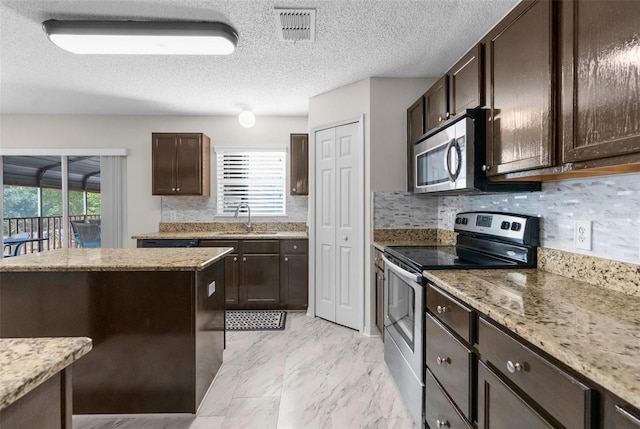 kitchen with a sink, visible vents, light stone countertops, dark brown cabinets, and appliances with stainless steel finishes