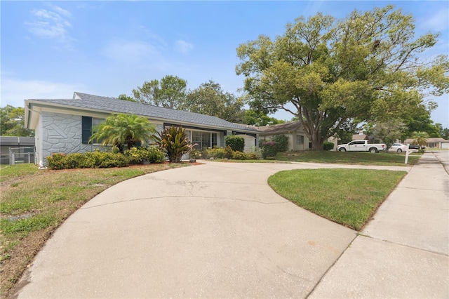 single story home with curved driveway, a front yard, and stone siding