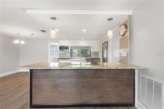 kitchen with appliances with stainless steel finishes, white cabinets, wood finished floors, a peninsula, and a chandelier