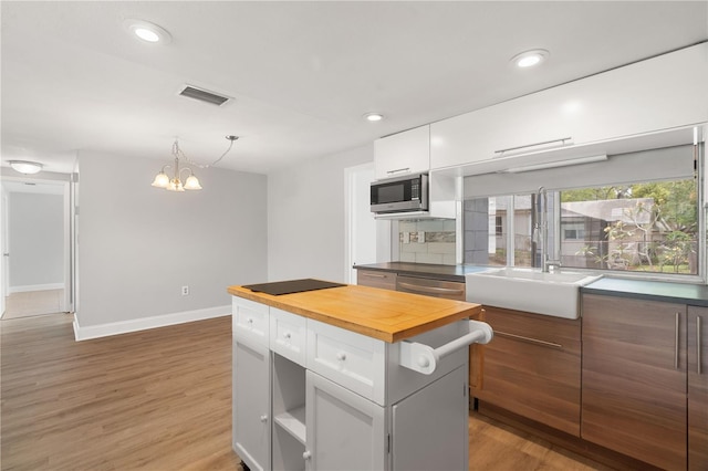kitchen with stainless steel microwave, butcher block countertops, white cabinetry, a chandelier, and recessed lighting