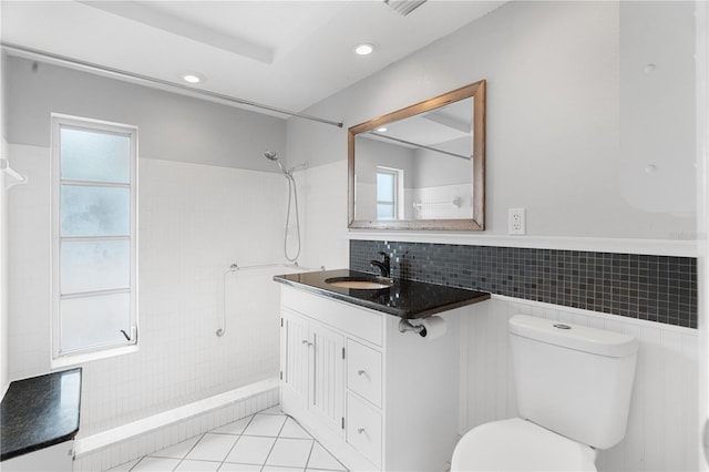 bathroom with toilet, tiled shower, tile patterned floors, tile walls, and vanity