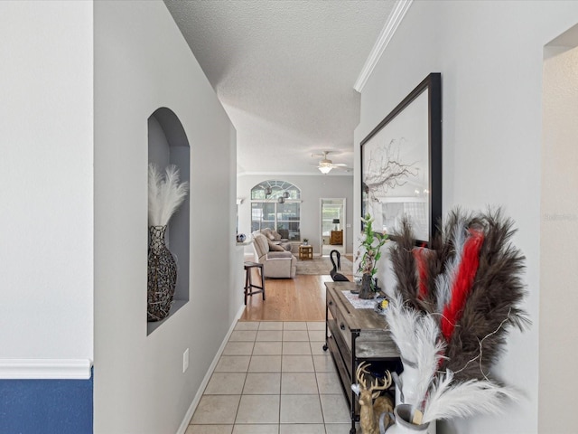 hallway featuring light tile patterned floors, ornamental molding, arched walkways, a textured ceiling, and baseboards