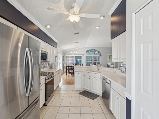 kitchen with appliances with stainless steel finishes, a sink, ornamental molding, white cabinetry, and vaulted ceiling
