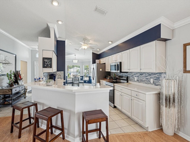 kitchen with appliances with stainless steel finishes, a kitchen breakfast bar, a peninsula, white cabinetry, and a ceiling fan