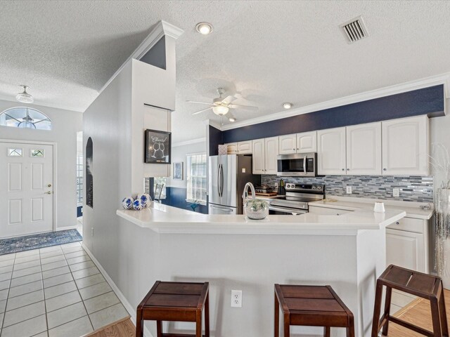 kitchen featuring appliances with stainless steel finishes, a textured ceiling, a kitchen bar, crown molding, and a ceiling fan
