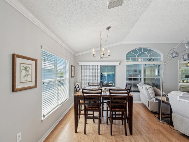 dining area with a chandelier, light wood-type flooring, ornamental molding, lofted ceiling, and a textured ceiling