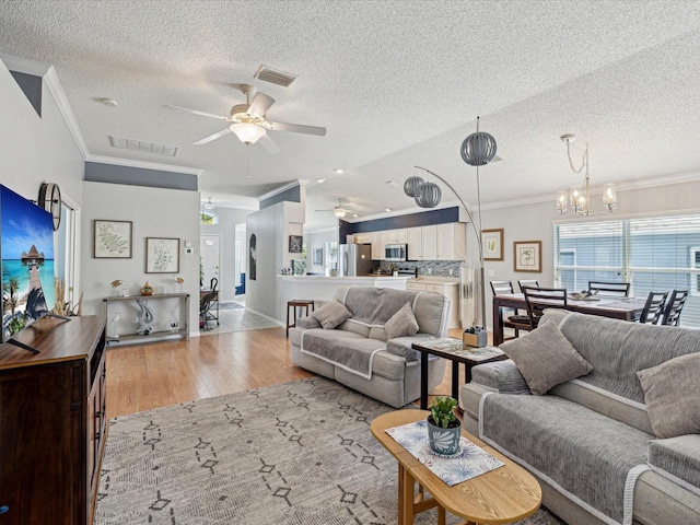 living area with a ceiling fan, ornamental molding, a textured ceiling, light wood-style floors, and a chandelier