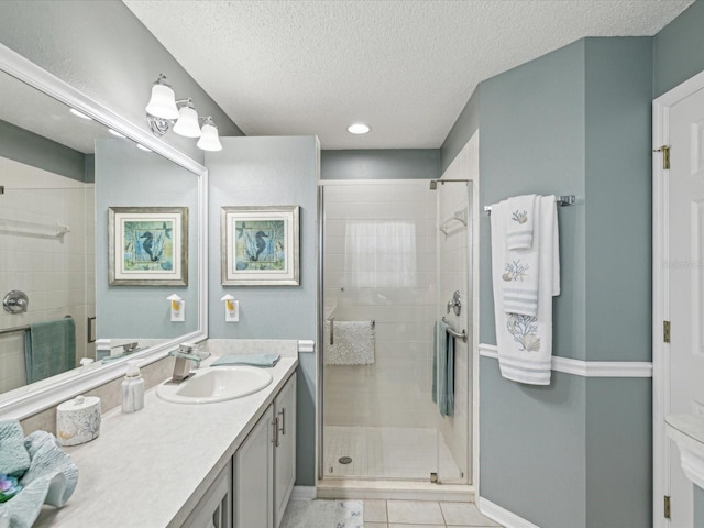 full bathroom featuring a shower stall, vanity, a textured ceiling, baseboards, and tile patterned flooring