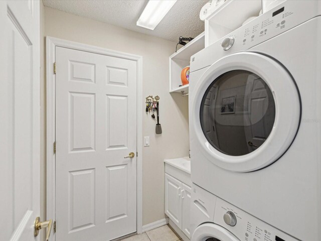washroom with stacked washer / drying machine, a textured ceiling, cabinet space, and light tile patterned flooring