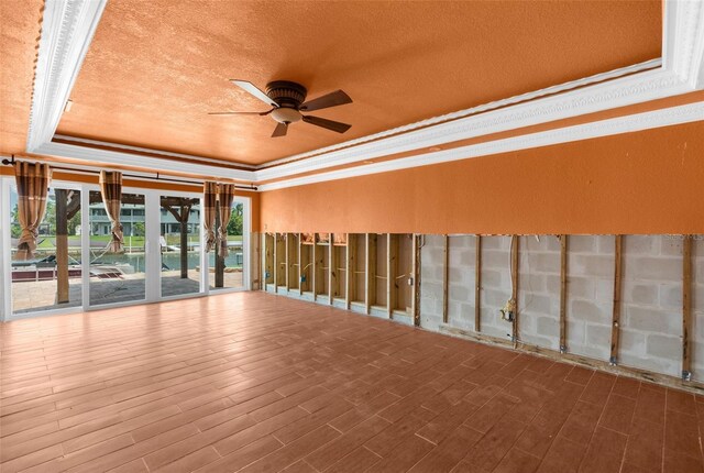 spare room with a raised ceiling, ceiling fan, crown molding, wood finished floors, and a textured ceiling