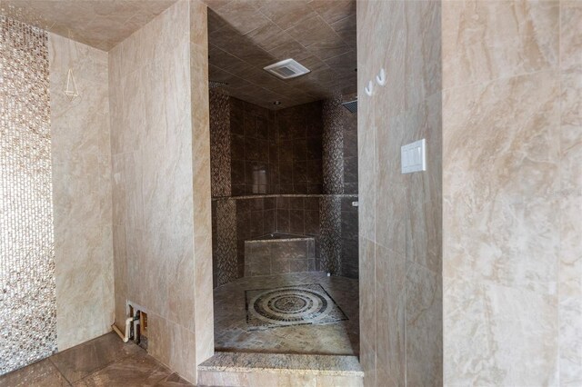 full bathroom with tiled shower and tile walls