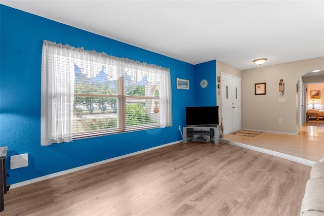 unfurnished living room featuring arched walkways, baseboards, and light wood-style floors