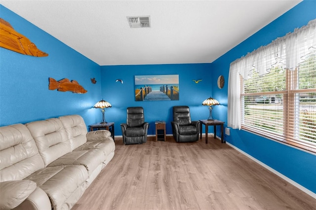 living room with an accent wall, baseboards, visible vents, and wood finished floors