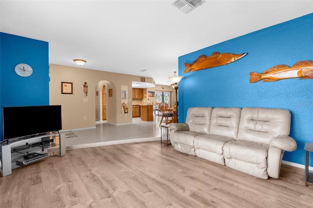 living room featuring arched walkways, baseboards, visible vents, and wood finished floors