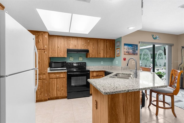 kitchen featuring black electric range oven, a peninsula, a sink, freestanding refrigerator, and under cabinet range hood