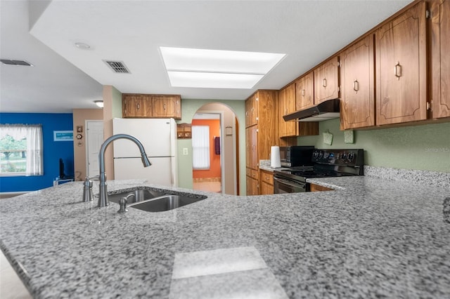 kitchen with a sink, brown cabinetry, visible vents, black appliances, and under cabinet range hood