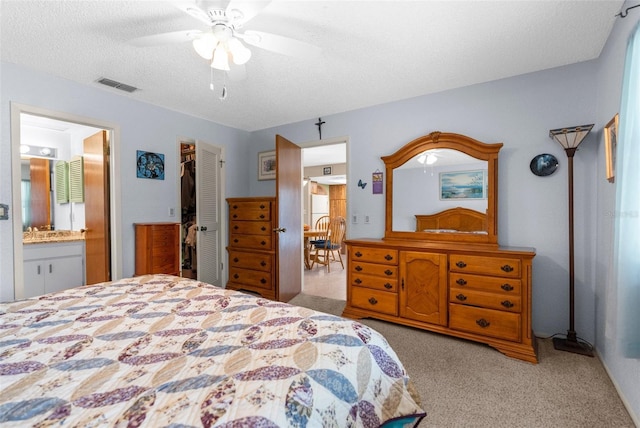 bedroom featuring a closet, a textured ceiling, carpet, visible vents, and connected bathroom