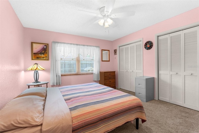 carpeted bedroom with a textured ceiling, a ceiling fan, and multiple closets