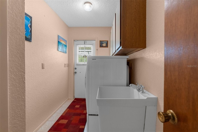 clothes washing area featuring washer / clothes dryer, a textured ceiling, baseboards, cabinet space, and a textured wall