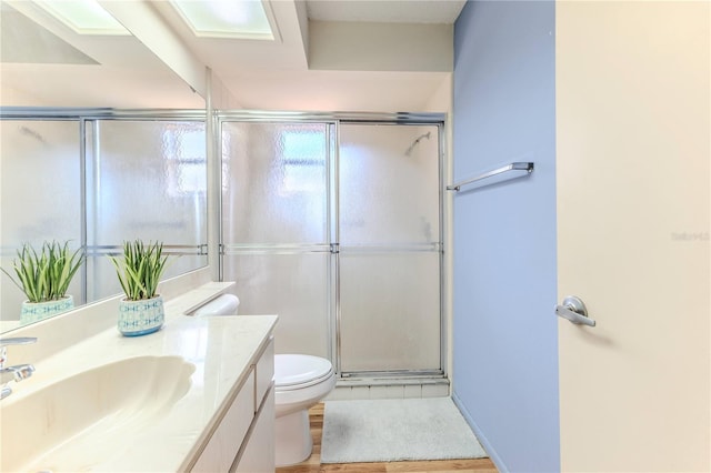bathroom featuring toilet, wood finished floors, vanity, and a stall shower