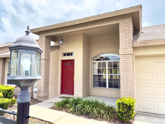 doorway to property with brick siding, stucco siding, and an attached garage