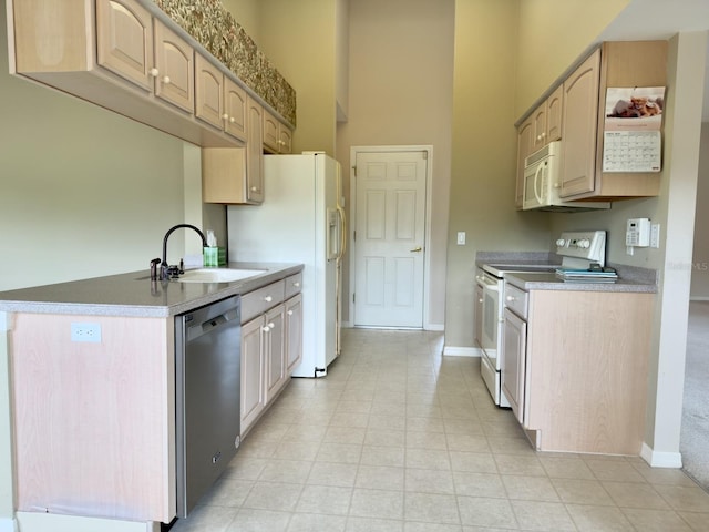 kitchen with white appliances, a sink, a towering ceiling, baseboards, and light tile patterned flooring