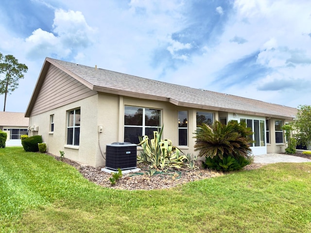 back of property with cooling unit, a yard, stucco siding, and a shingled roof