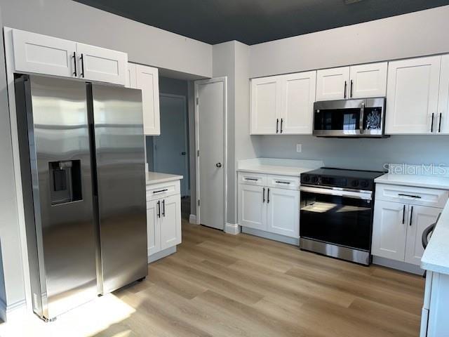 kitchen with stainless steel appliances, light countertops, white cabinets, and light wood-style floors