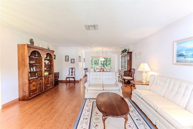 living room featuring light wood-style flooring, a textured ceiling, and baseboards