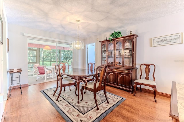 dining area with a textured ceiling, light wood-type flooring, a chandelier, and baseboards