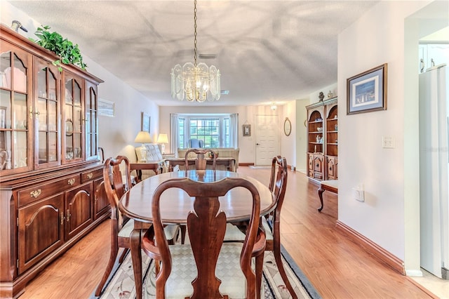 dining room with light wood-style flooring, a chandelier, baseboards, and a textured ceiling