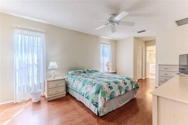 bedroom featuring light wood finished floors, a textured ceiling, ceiling fan, and ensuite bath